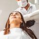 A dental technician prepares to take an X-ray of a woman sitting in a dental chair.