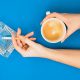 A person holds a cup of coffee in one hand and a lit cigarette over an ashtray in the other, against a blue background.