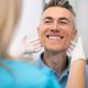 A healthcare professional wearing gloves examines a smiling man’s jawline and neck during a medical checkup.