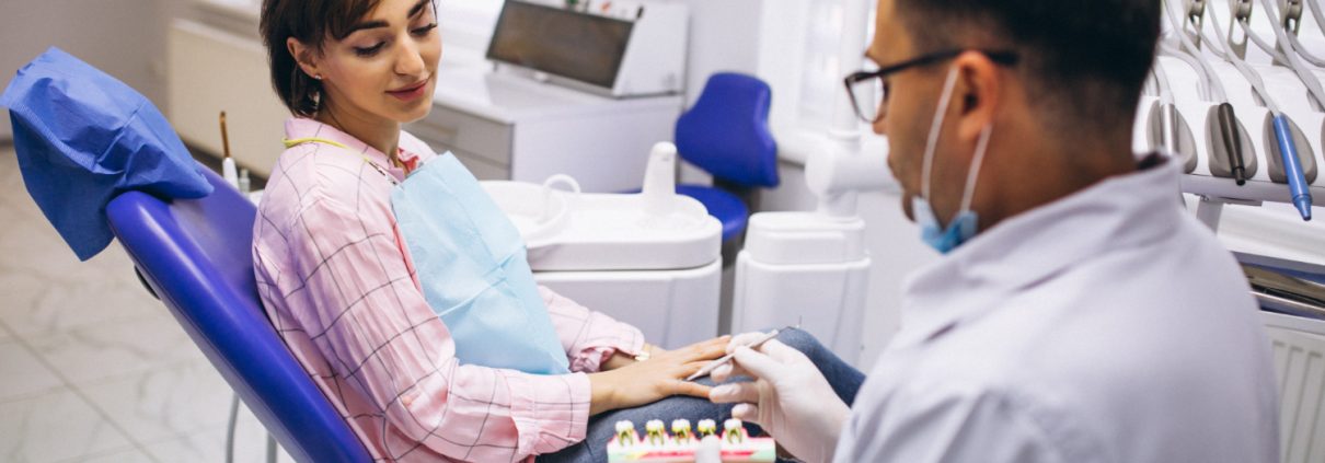 A dentist shows a dental model to a woman sitting in a dental chair during a consultation in a modern dental clinic.