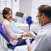A dentist shows a dental model to a woman sitting in a dental chair during a consultation in a modern dental clinic.