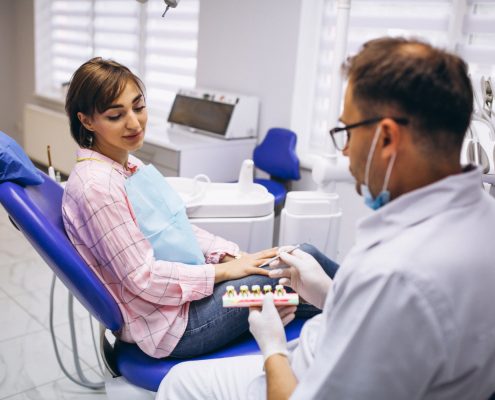 A dentist shows a dental model to a woman sitting in a dental chair during a consultation in a modern dental clinic.